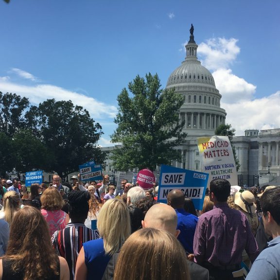 Photo of protesters in front of a Capitol building holding signs that read "SAVE MEDICAID"